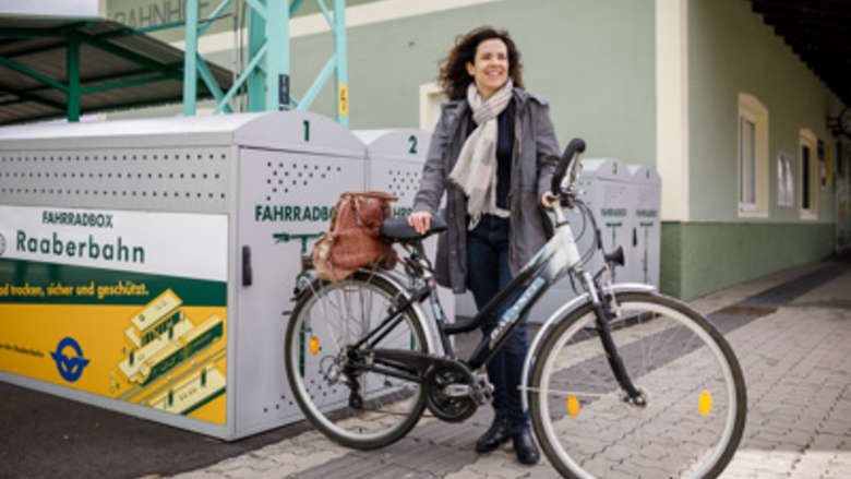 Frau mit Fahrrad vor Radboxen auf Bahnhof